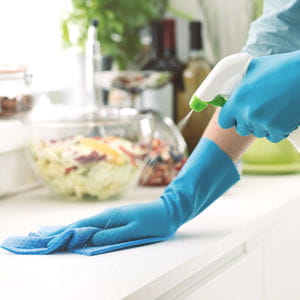 Gloved hand wiping a kitchen counter, room-by-room cleaning tips and checklists.