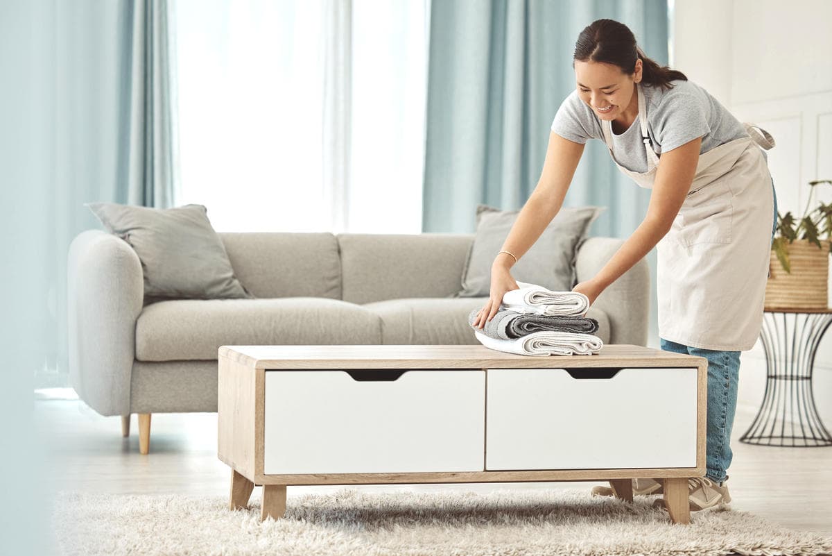 Person folding clean towels on a coffee table in a tidy living room, representing everyday home care and professional cleaning routines.