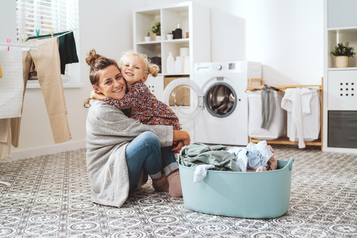 Parent and child sitting beside a laundry basket in a bright home laundry room, representing everyday cleaning routines and family-friendly home care.