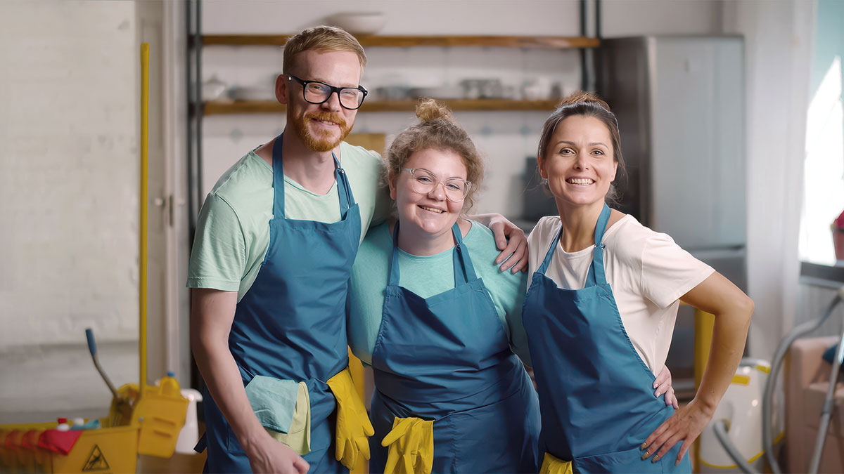 Three uniformed cleaning team members pose together with gloves and aprons, representing a coordinated, professional cleaning crew.